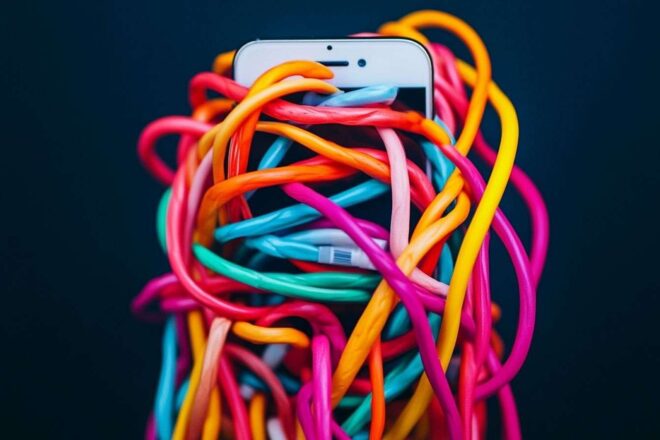 Image artistique d'un smartphone embrouillé dans des câbles multicolores sur un fond obscur.